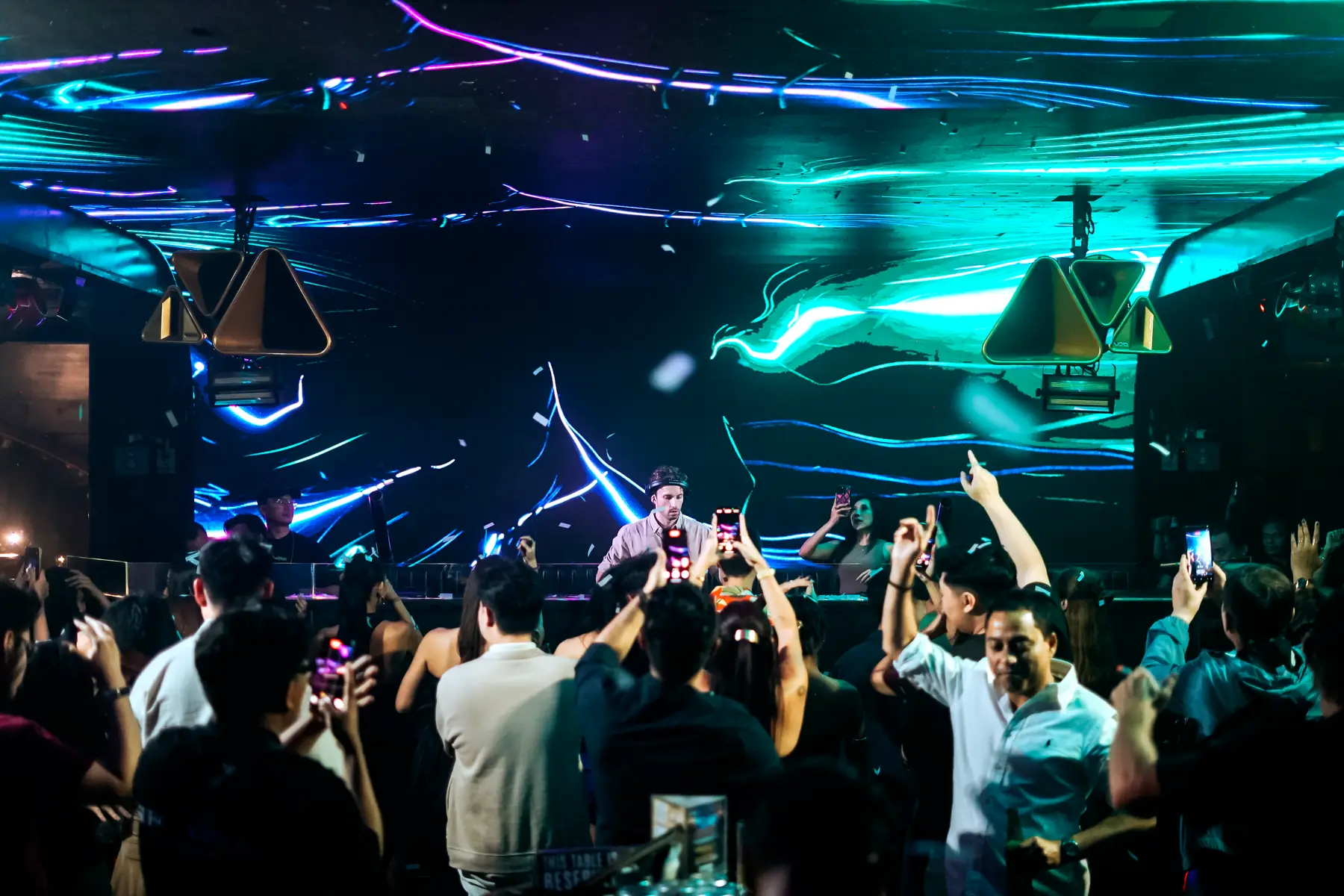 A packed floor with phones raised, Arensky playing on the booth under blue and green lasers