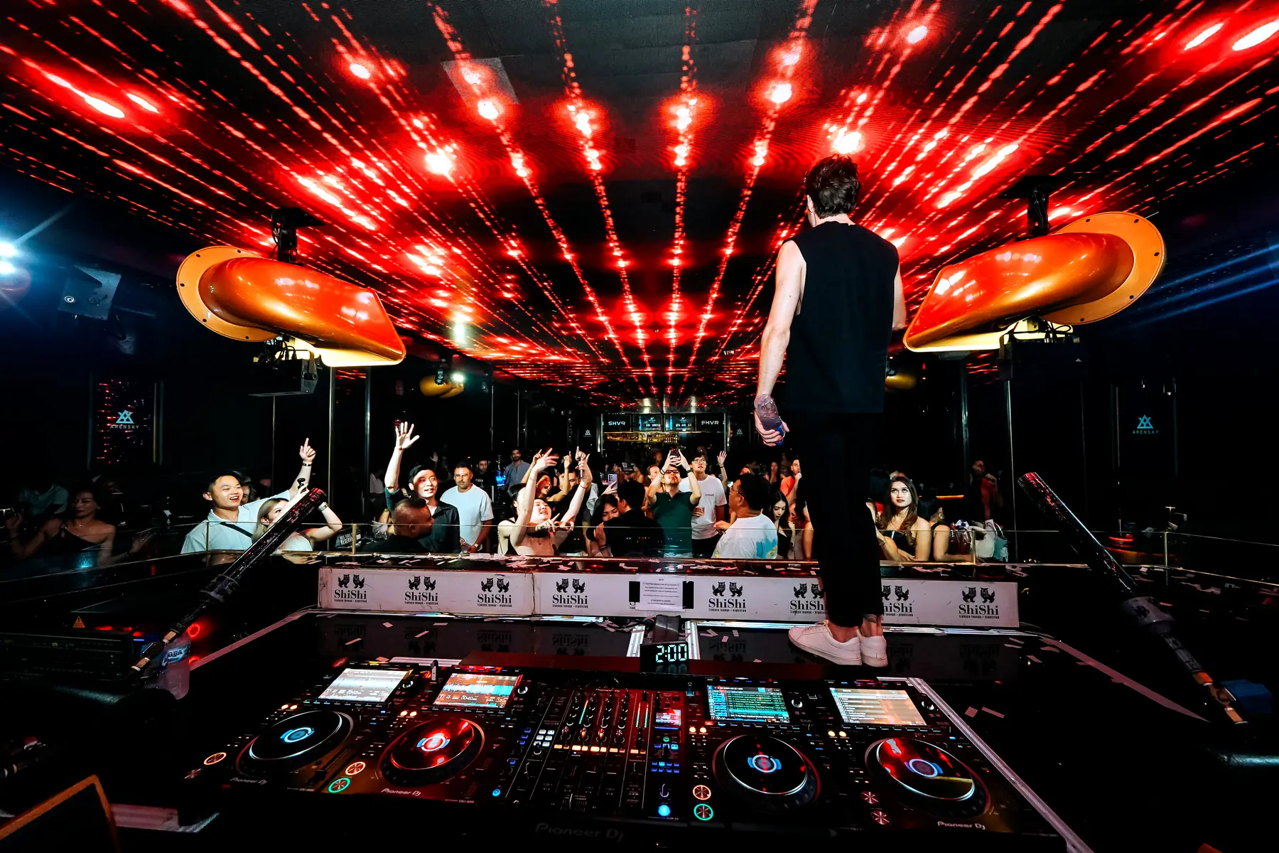 Arensky standing on the booth at ShiShi Bali, red lights across the ceiling and the crowd below